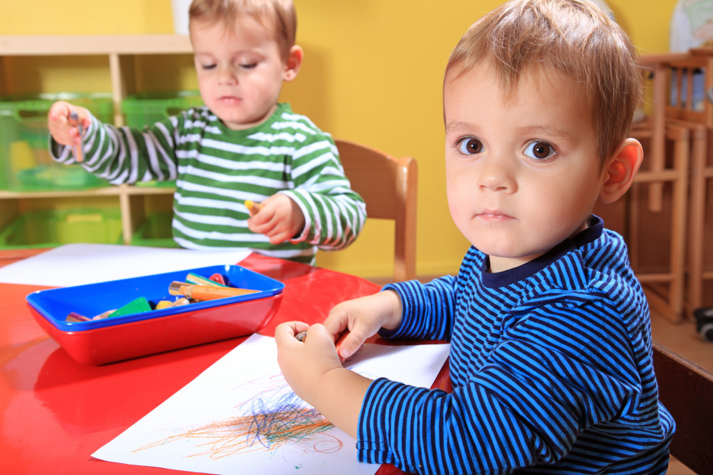 Two children using colors to draw on paper