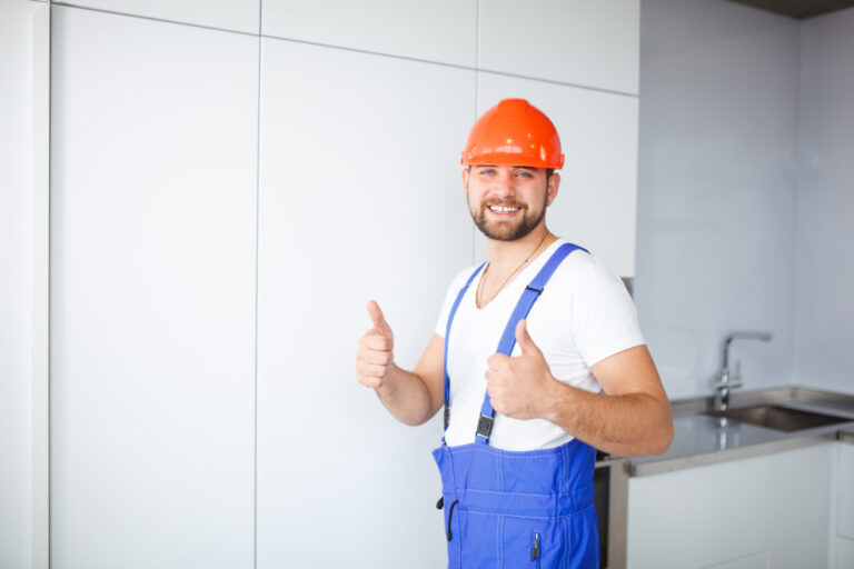 a maintenance worker wearing ppe doing an okay sign in front of a kitchen sink