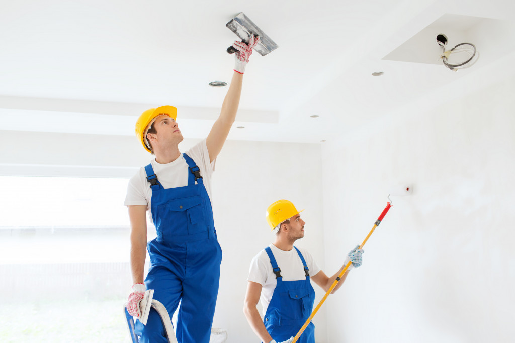 two painters in uniform and wearing hard hats painting the wall and the ceiling with white paint
