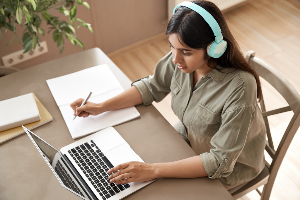 Young woman working remotely using a laptop and headset.