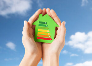 A hand holding a green-colored cardboard house with energy rating
