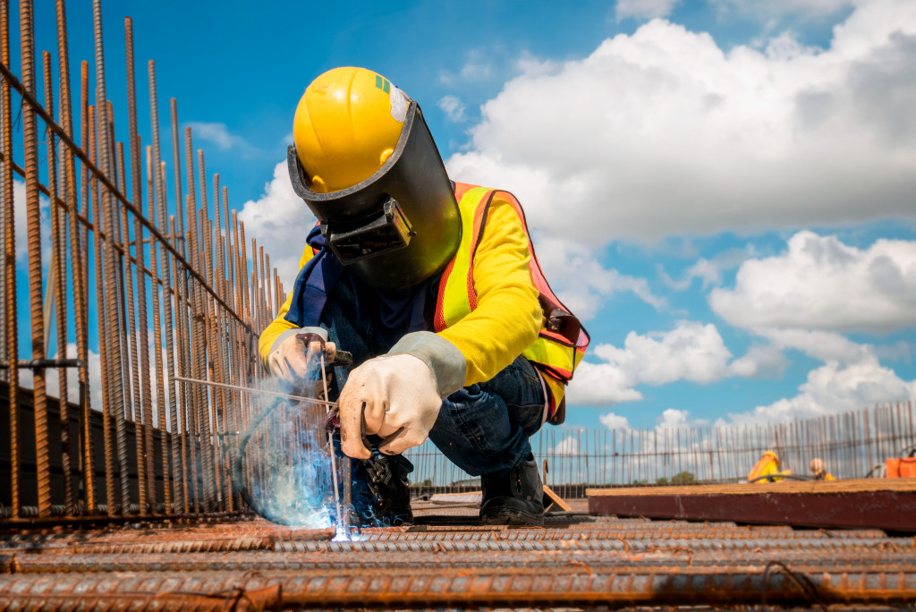 Construction worker welding steel at a construction site while wearing safety equipment.
