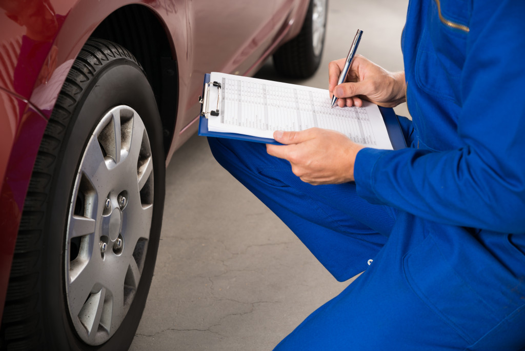 mechanic in blue uniform inspecting the car with checklist on clipboard