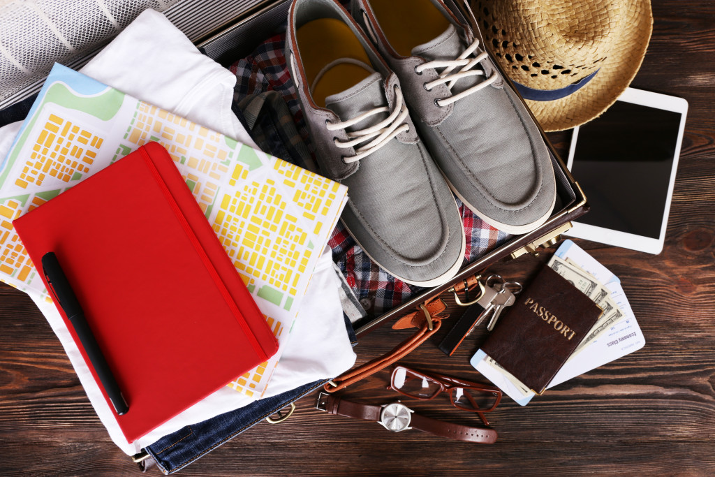 Packed suitcase of a tourist with travel items on a wooden table.
