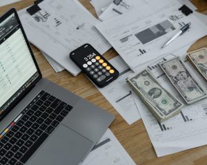 dollar bills, a calculator, documents, and a laptop